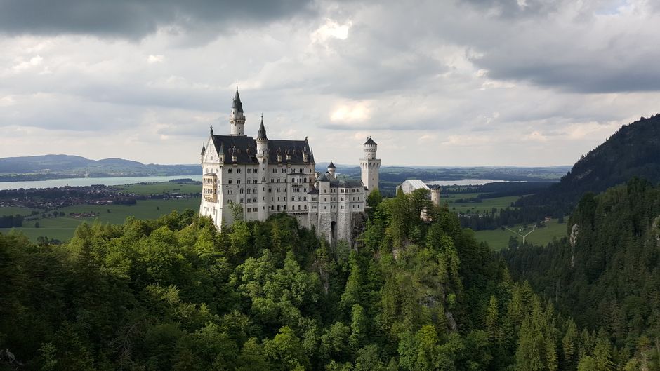Explore the breathtaking view of Neuschwanstein Castle surrounded by lush greenery and scenic hills.