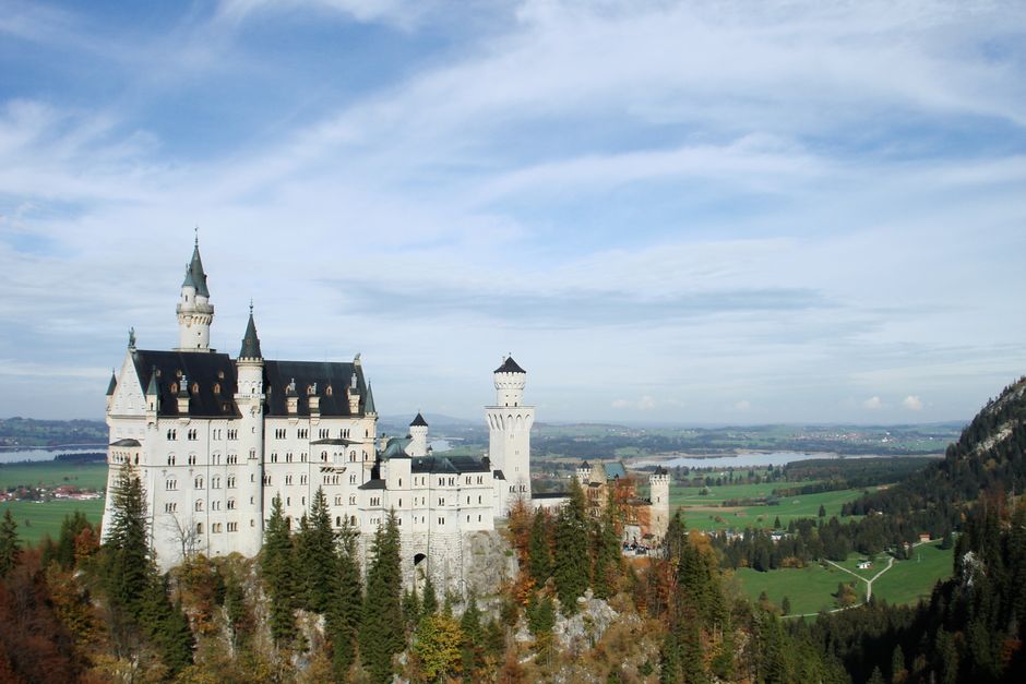 View of Neuschwanstein Castle in Schwangau, Bavaria, surrounded by lush landscape.