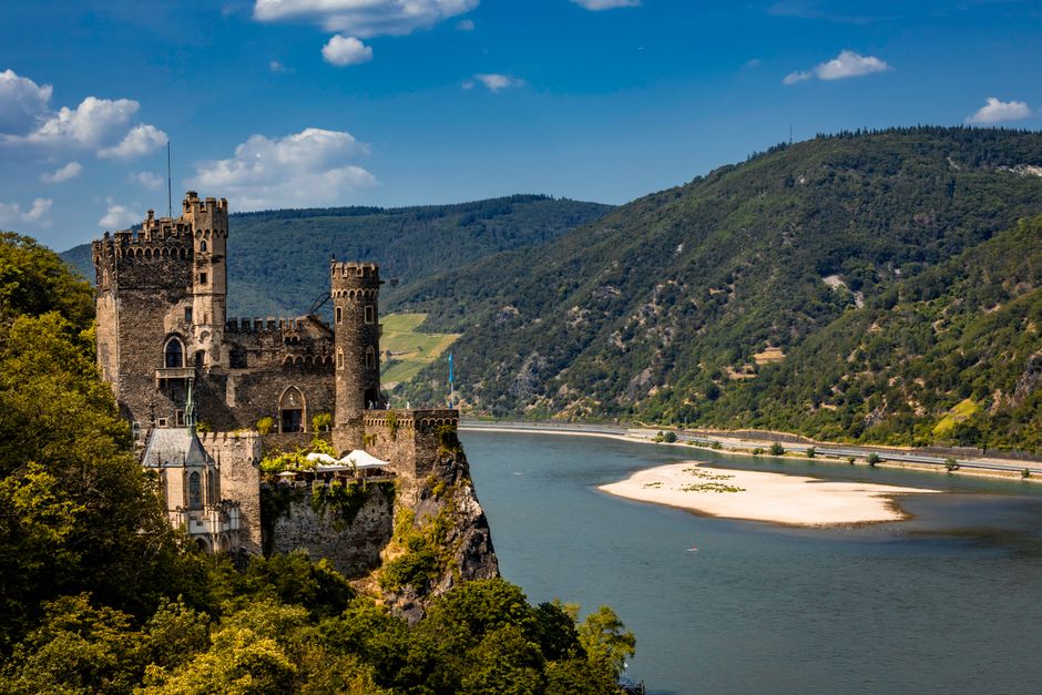 Rheinstein Castle set against a scenic backdrop of the Rhine River in summer.